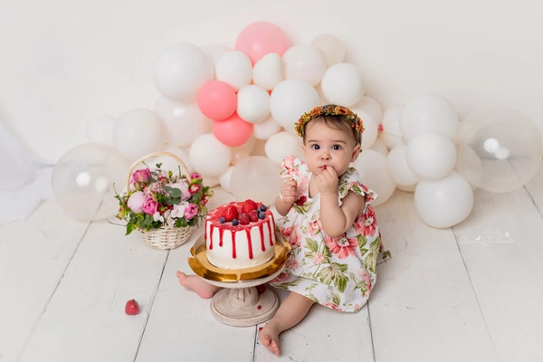 Baby girl with a birthday cake and pink balloons