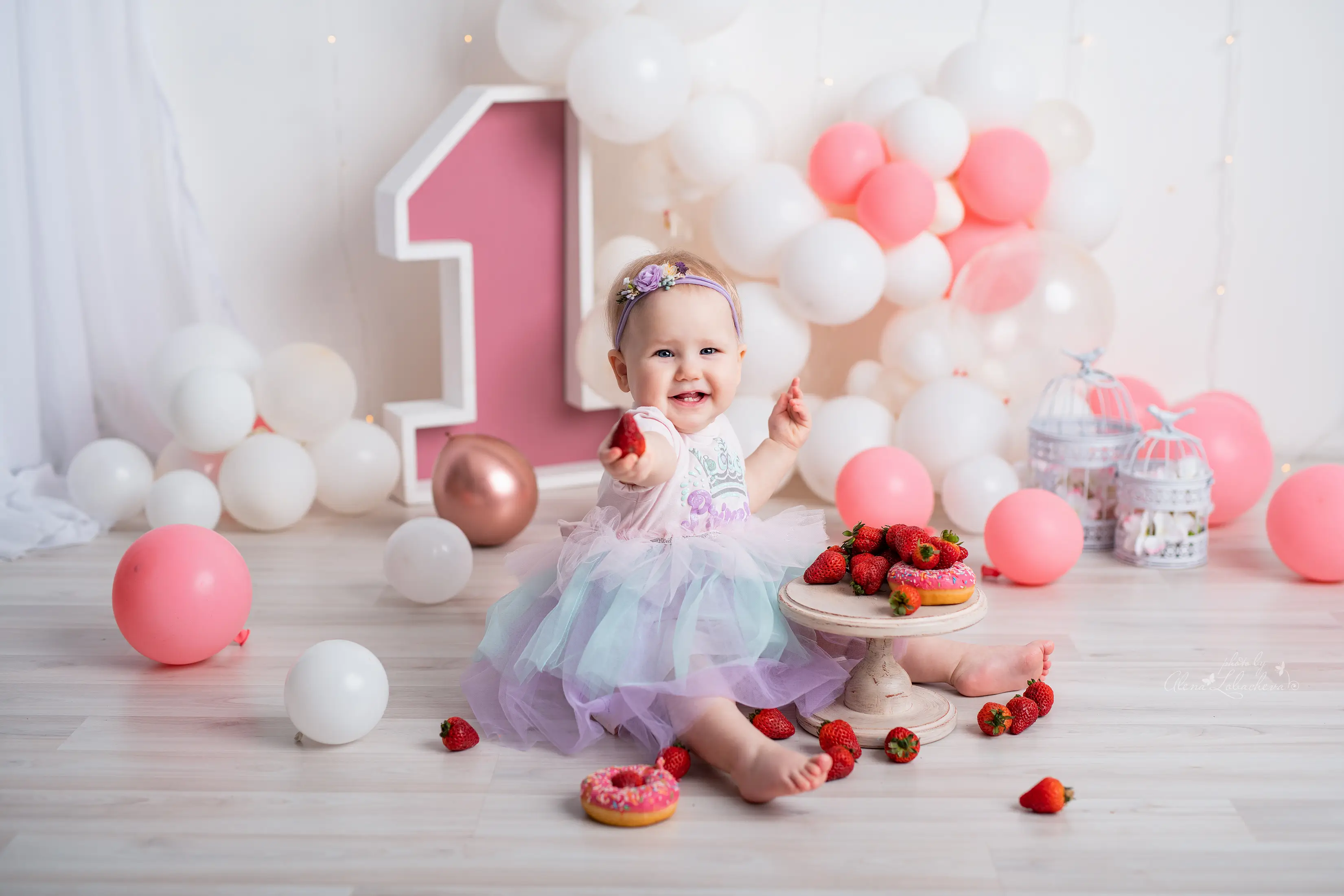 Smiling baby celebrating a first birthday in a strawberry studio setup