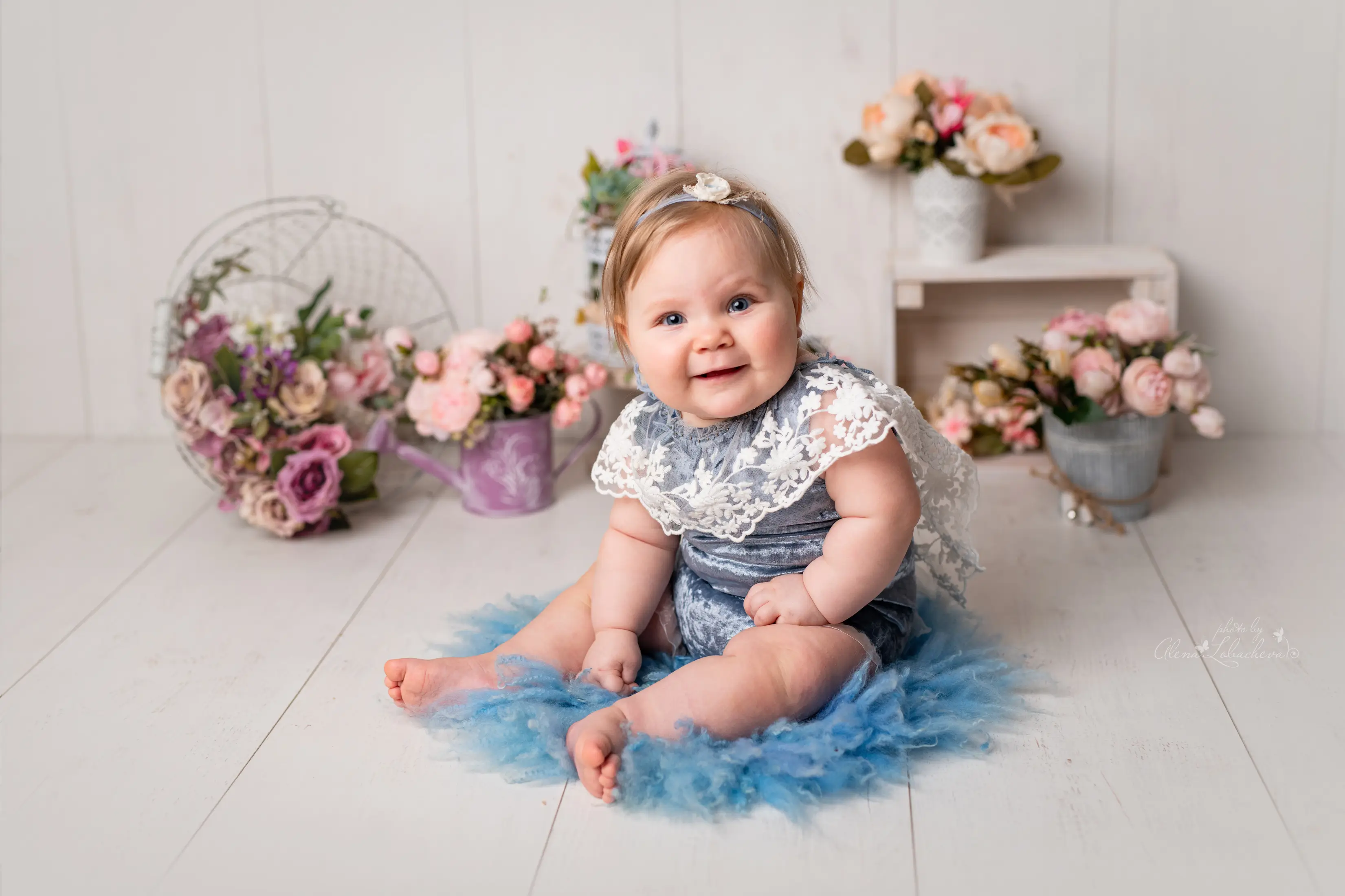 Smiling sitter-age baby in a blue floral studio setup