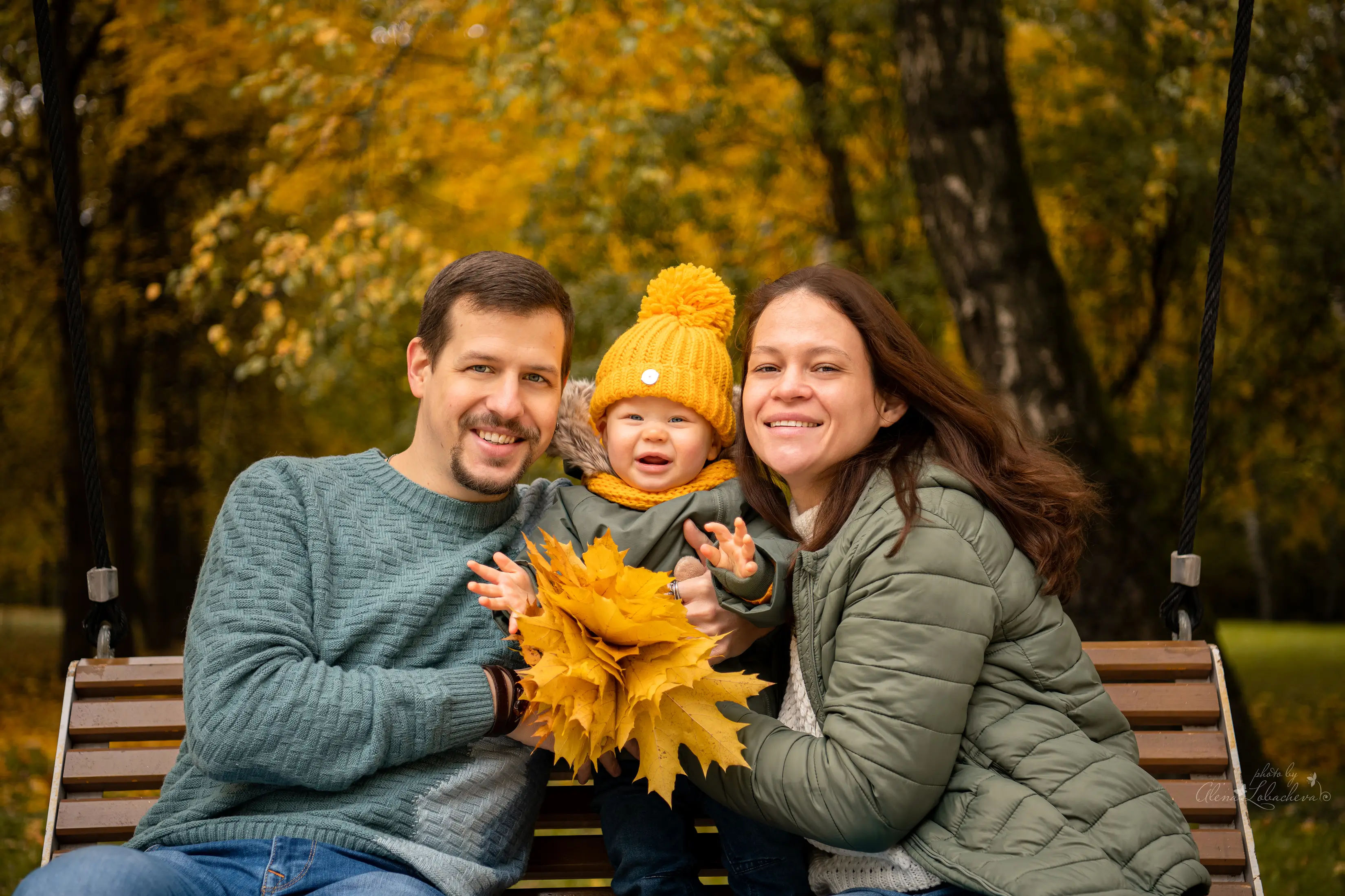 Parents and baby smiling together on a park bench in autumn