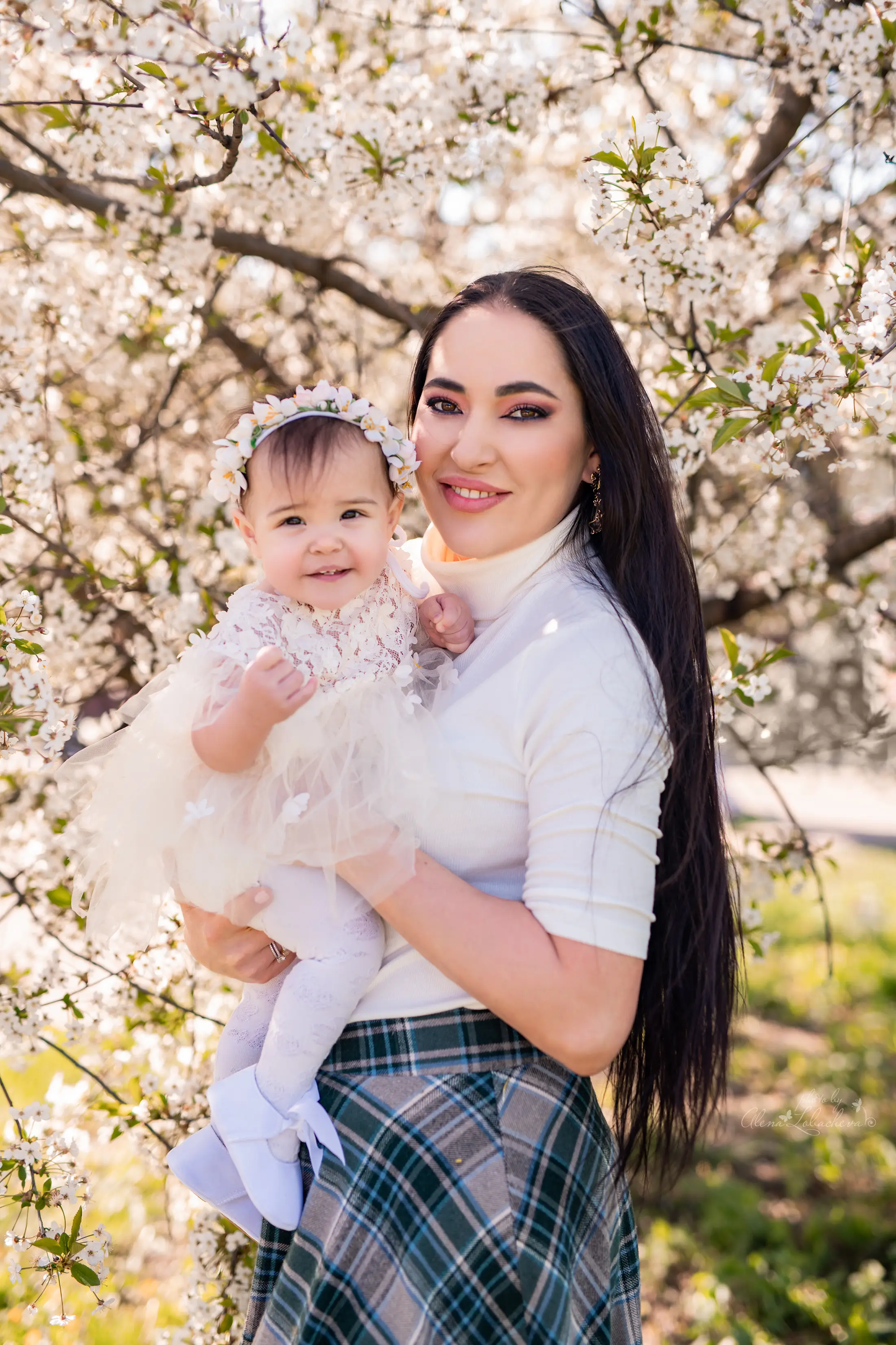 Mother holding her baby beneath spring blossoms during a family session