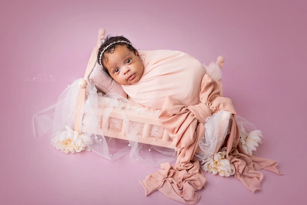 Awake newborn baby wrapped in soft pink fabric