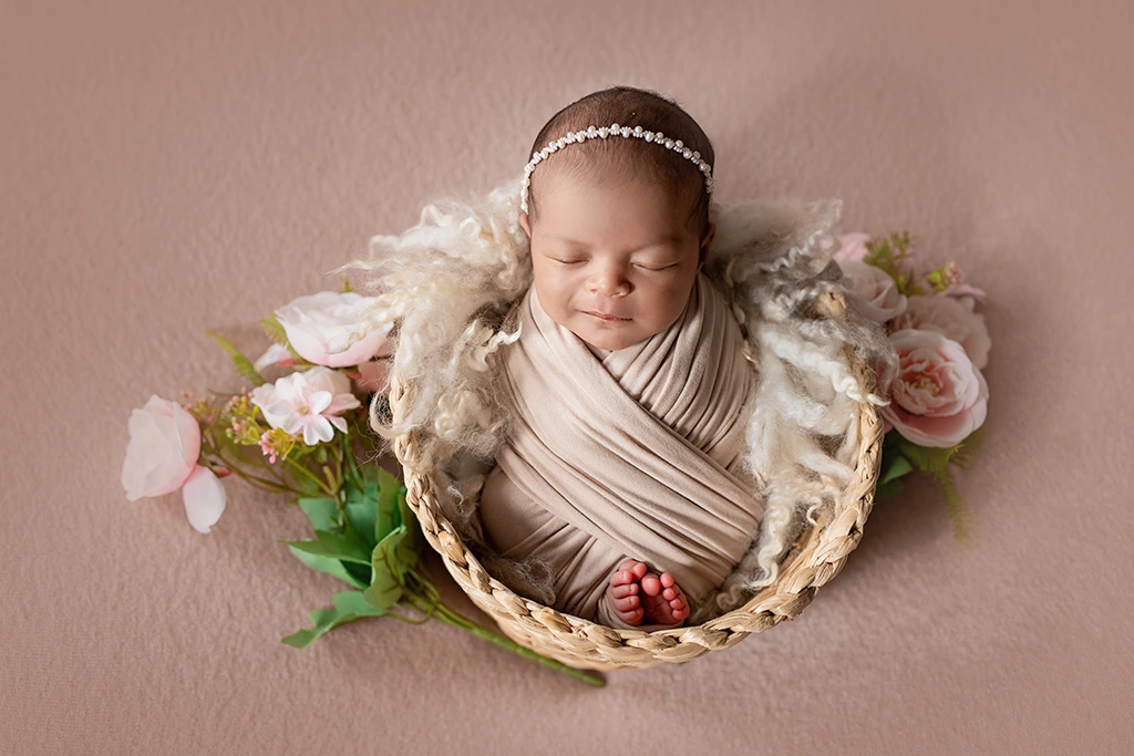 Wrapped newborn baby girl posed in a floral basket