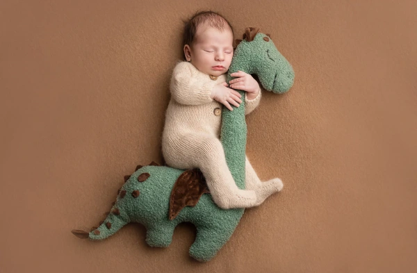 Sleeping newborn baby posed with a green dinosaur prop
