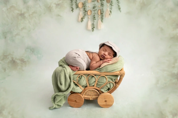 Sleeping newborn baby posed in a green wooden stroller