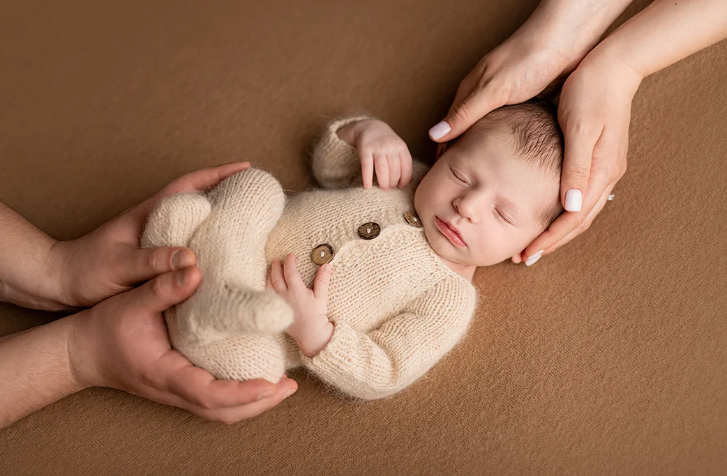 Newborn baby supported by adult hands during a safe posed photography setup