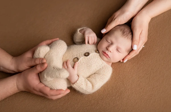 Newborn baby supported by adult hands during a posed portrait