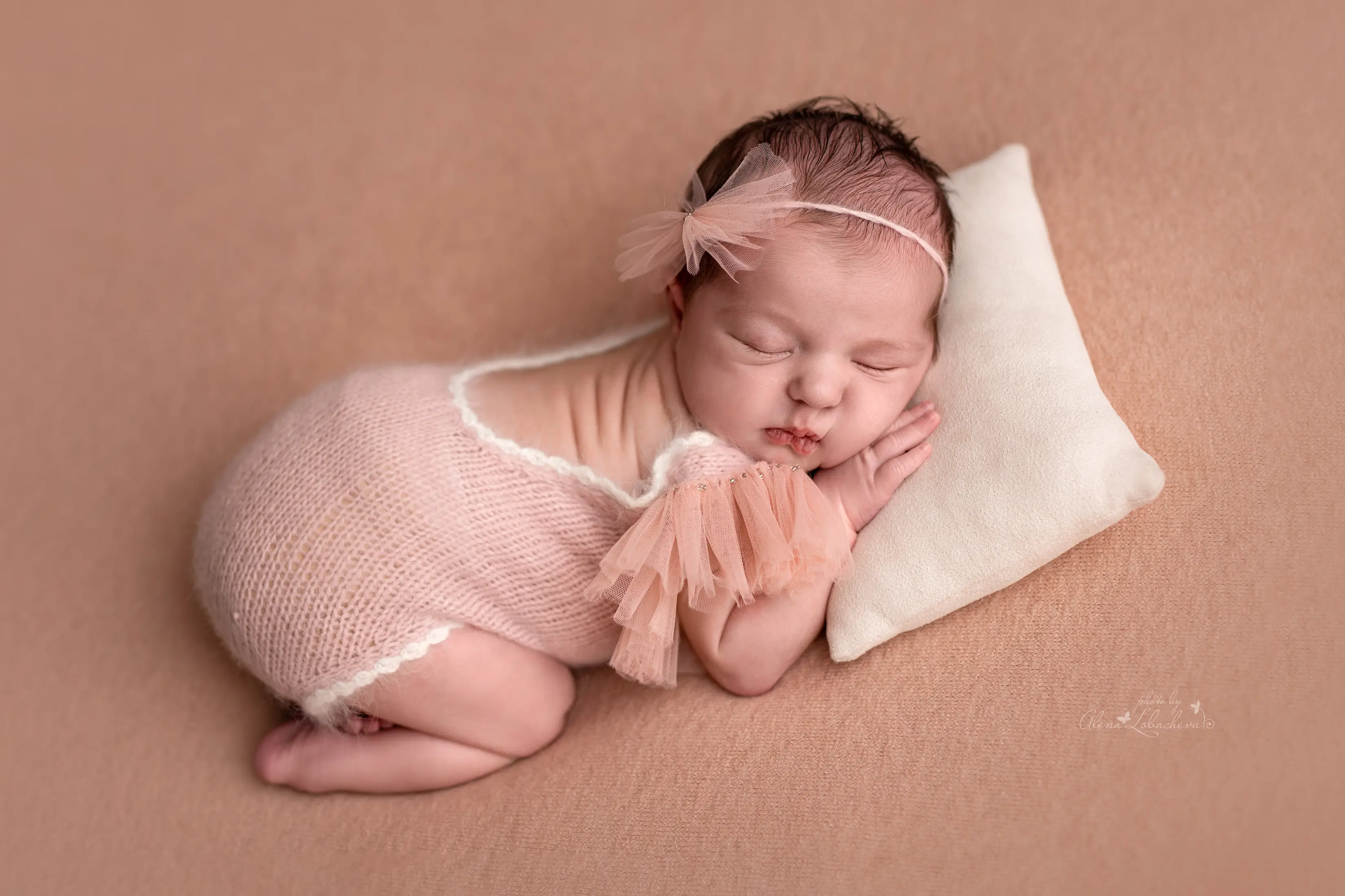 Newborn baby posed in a soft pink studio setup