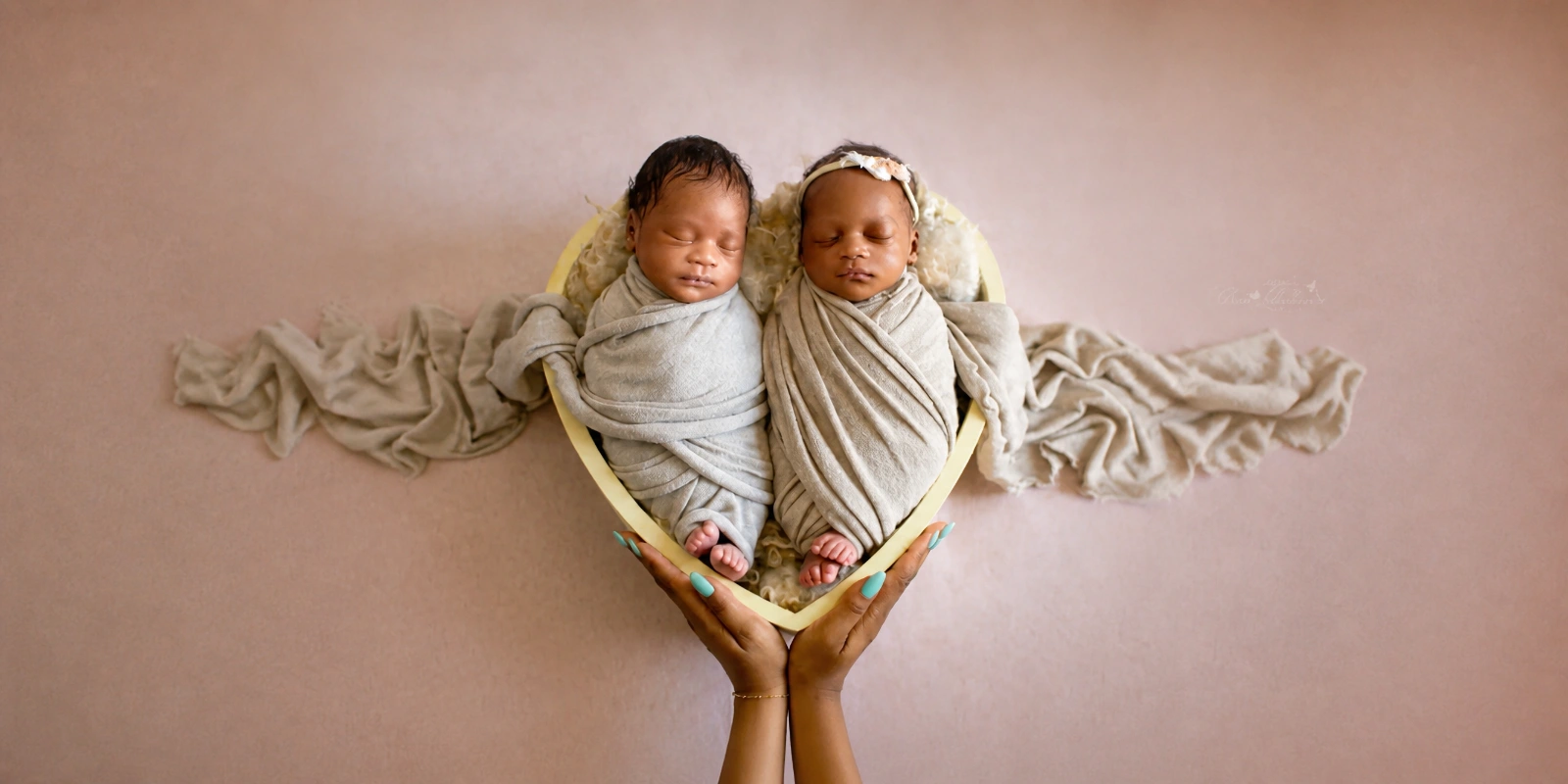 Sleeping newborn twins wrapped in neutral blankets inside a heart-shaped prop